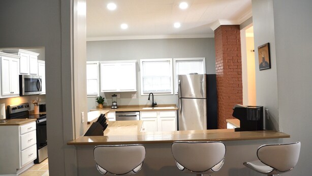 Une cuisine moderne avec des meubles blancs, des appareils en acier inoxydable et un îlot central doté de tabourets de bar.