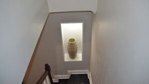 Un escalier avec une petite fenêtre derrière laquelle on aperçoit un vase.