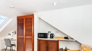 Una habitación compacta con tragaluces, un escritorio con silla, microondas y una pequeña zona de kitchenette.