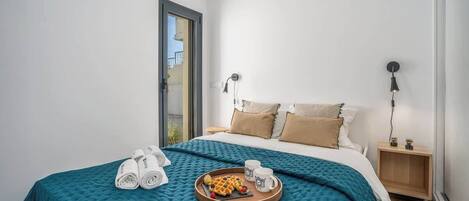 Habitación de hotel con cama, bandeja de waffles y fruta, toallas y mesita de noche con lámpara.