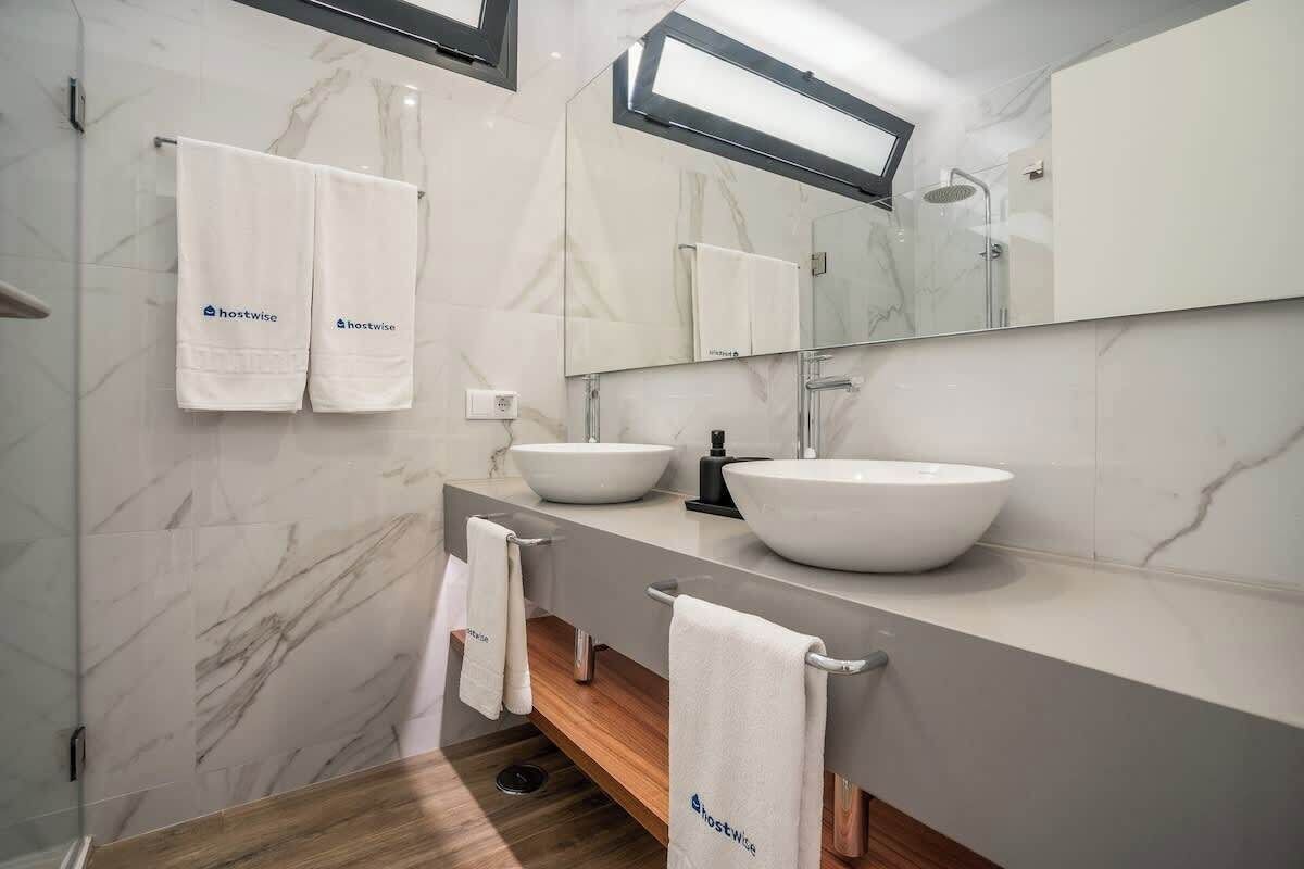 A modern bathroom with two white sinks, a large mirror, and marble walls.