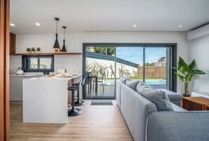 A modern kitchen with a central island, a dining area with chairs, and a large sliding glass door leading to a pool area. - Bright Spacious House | Swimming Pool by HostWise (Porches)