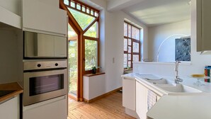 Eine moderne Küche mit Holzboden, eingebauten Backöfen, einem großen Fenster und einer weißen Arbeitsplatte.