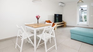 Un salon moderne avec une table à manger en bois, des chaises blanches, un canapé de couleur turquoise, un téléviseur à écran plat et une grande fenêtre.