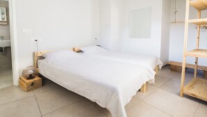 Une chambre à coucher au style minimaliste, avec un lit simple, une table de chevet en bois, une petite table d’appoint et une étagère en bois.