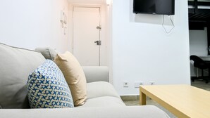 A living room with a sofa, a coffee table, a TV mounted on the wall, and a door leading to another room. - M (RVI40) Cozy one-bedroom apartment in Cuatro Caminos (Madrid)