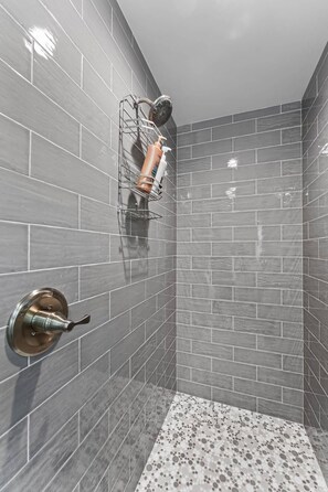 Eine Dusche mit grauen Fliesen, einem Duschkopf und einer Seifenspender.