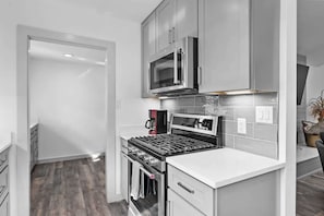 Una cucina moderna con elettrodomestici in acciaio inossidabile, mobili bianchi e una parete di fondo piastrellata.