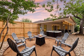 Ein Garten mit Feuerstelle, Gartenmöbeln, Whirlpool und überdachter Terrasse.
