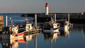 A harbor with boats docked at a pier, a lighthouse in the background, and calm water reflecting the boats. - Charming studio near La Cotinière Port - 2 pax, Parking (Saint-Pierre-d'Oléron-La Cotinière)