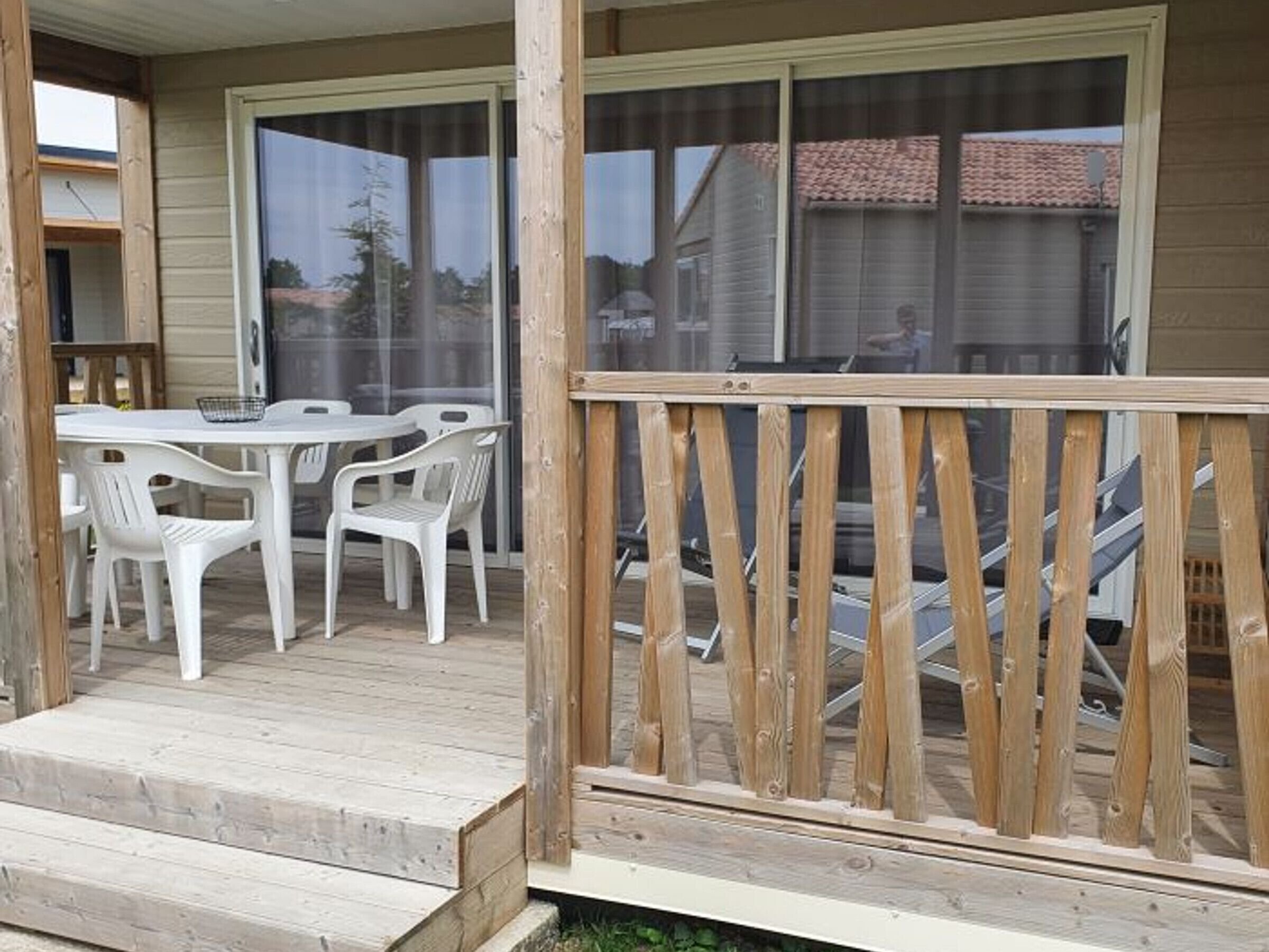 Un patio couvert avec une terrasse en bois, une table et des chaises, et une porte-fenêtre coulissante donnant sur la maison.
