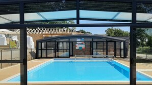 Ein überdachter Schwimmteich mit Glasverkleidung, einer Bedienkonsole und einer Holzterrasse.