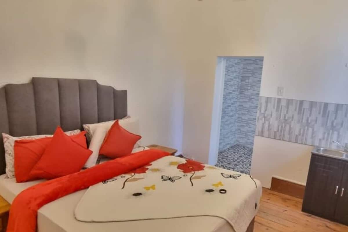 A bedroom with a bed, pillows, a nightstand, a wooden floor, a wardrobe, and a wall-mounted TV.