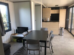 A modern kitchen with wooden cabinets, a dining area with a table and chairs, and a television on a small stand. - 3-bedroom chalet, pool, 100m from lake - Olonzac (Olonzac)