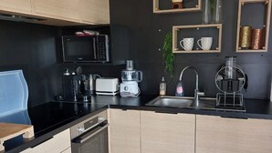 A modern kitchen with a black countertop, wooden cabinets, a microwave, a coffee machine, a toaster, and a sink. - 3-bedroom chalet with terrace in green setting (Marzan)