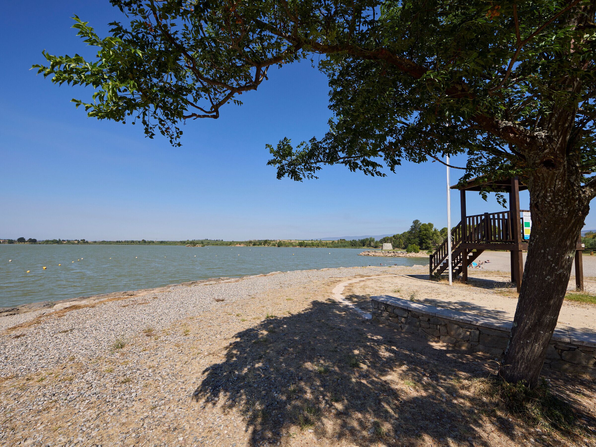 Une plage avec un kiosque en bois, un ciel dégagé et une eau calme.