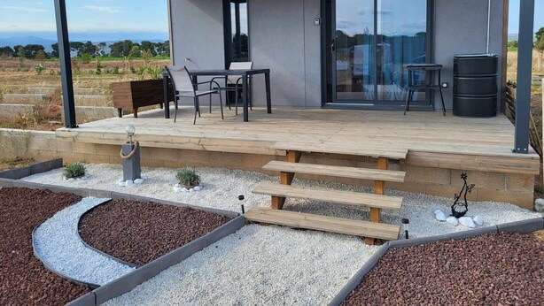 A modern outdoor patio with a table and chairs, a wooden deck, and a garden area with gravel and plants.