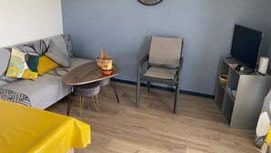 A modern living room with a sofa, a dining table, a chair, and a TV stand.
