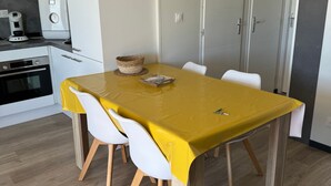 A dining area with a yellow table, white chairs, a basket, and a remote control.