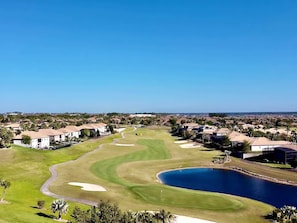Un campo de golf con un estanque, rodeado de edificios residenciales.