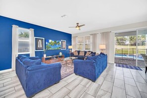 A living room with blue walls, a ceiling fan, a sofa set, a coffee table, and a view of a swimming pool.