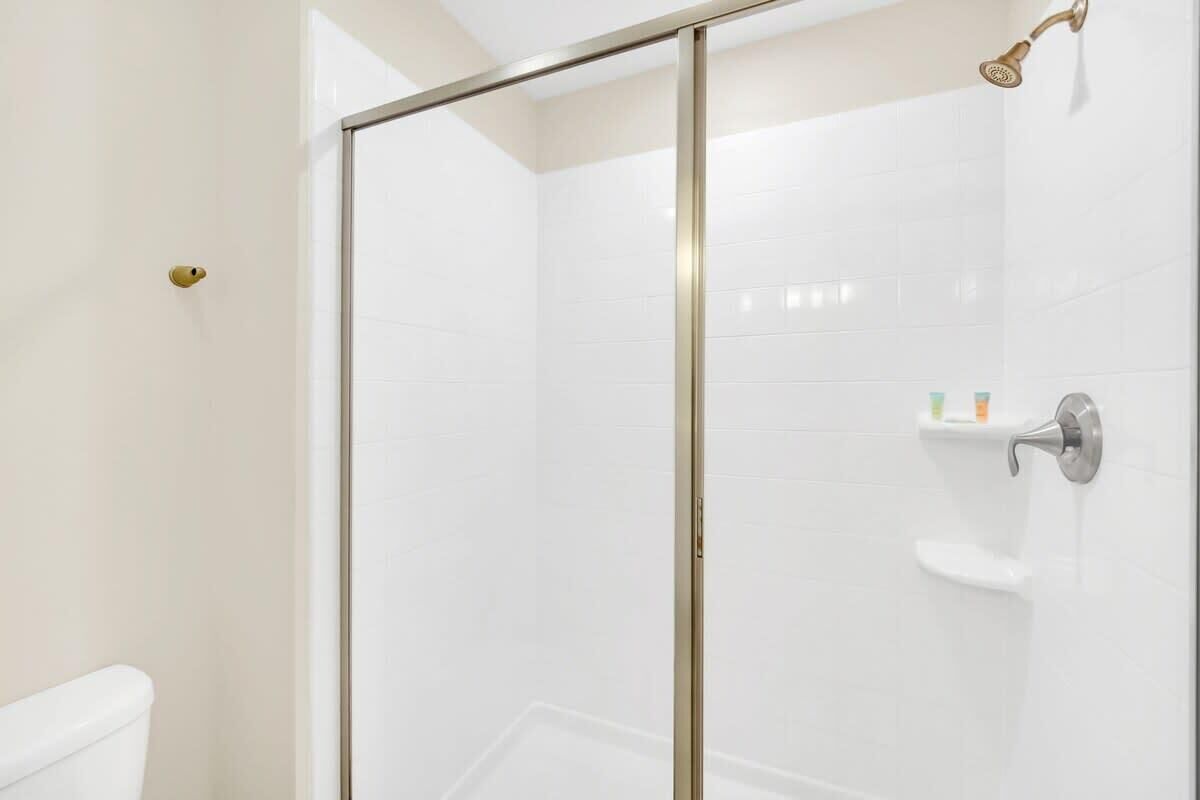 Un baño moderno con cabina de ducha de vidrio, azulejos blancos y un inodoro.