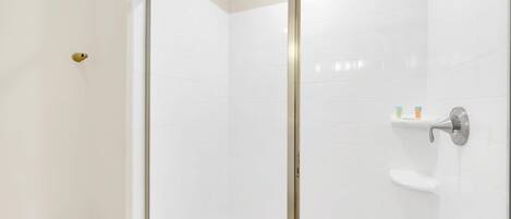 Un baño moderno con cabina de ducha de vidrio, azulejos blancos y un inodoro.