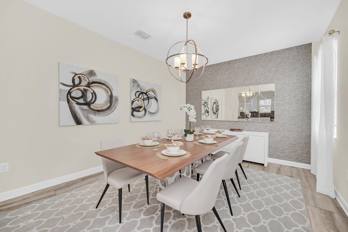 Un coin repas avec une table en bois dressée pour six personnes, des chaises blanches et des œuvres d’art abstraites accrochées au mur.