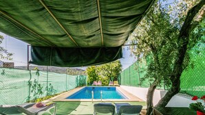 A swimming pool with a green canopy overhead, surrounded by white lounge chairs and a tree. - Beautiful home in Alcala la Real (Alcala la Real)