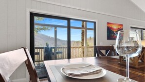 Comedor con una mesa dispuesta para dos, un vaso de agua y vistas a un paisaje montañoso a través de amplios ventanales.