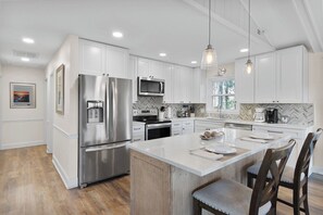A modern kitchen with white cabinetry, stainless steel appliances, a herringbone tile backsplash, and a central island with seating. - Cozy Bungalow - Big Views, Pool & 4 Master Suites (Dillard)