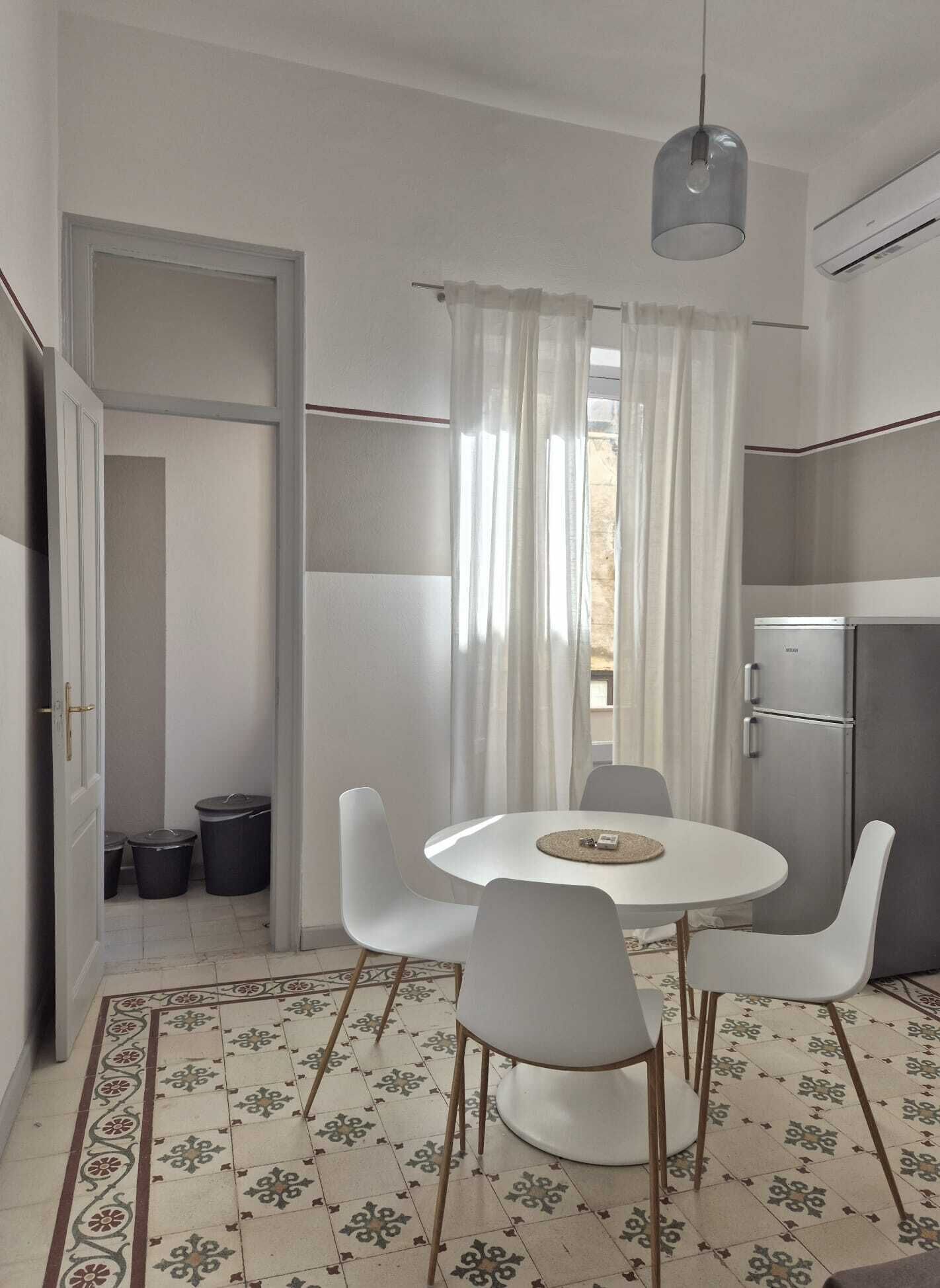 Cocina compacta con zona de comedor, refrigerador y ventana con cortinas.