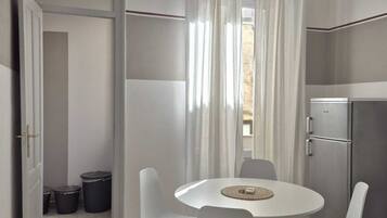 Cocina compacta con zona de comedor, refrigerador y ventana con cortinas.
