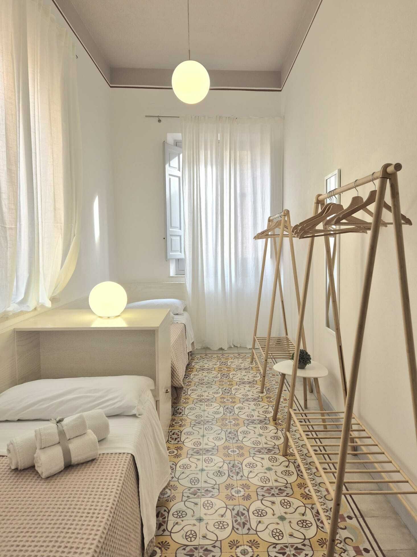 A bedroom with a bed, a bedside table with a lamp, a wooden drying rack, and patterned floor tiles.