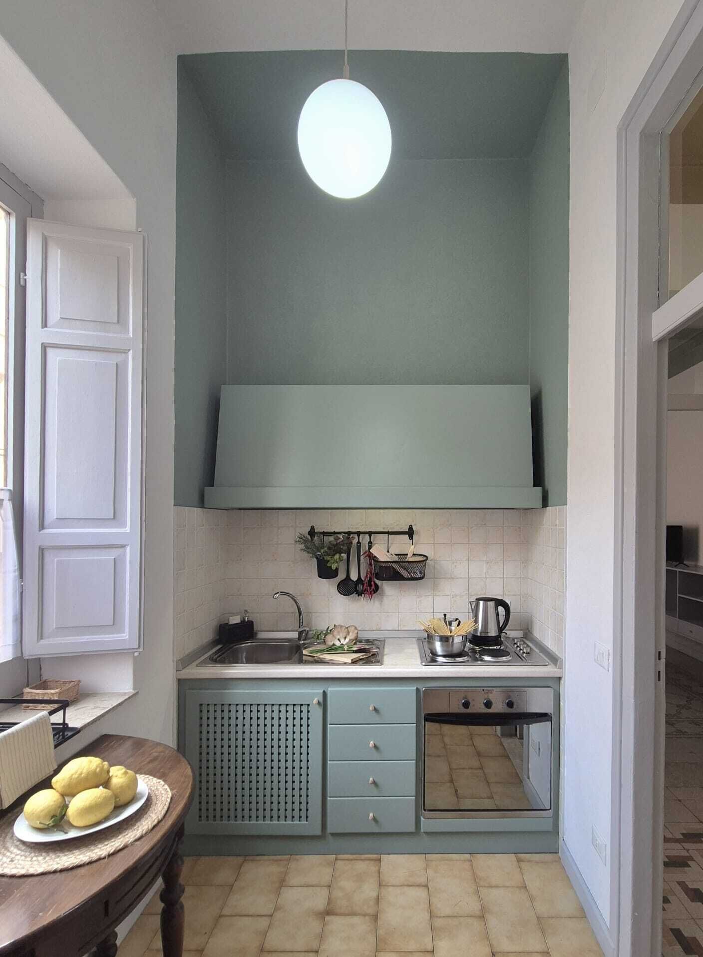 Una cucina compatta con piano di lavoro bianco, lavello, fornello e lampada a sospensione.