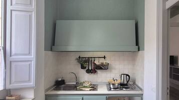 Una cucina compatta con piano di lavoro bianco, lavello, fornello e lampada a sospensione.