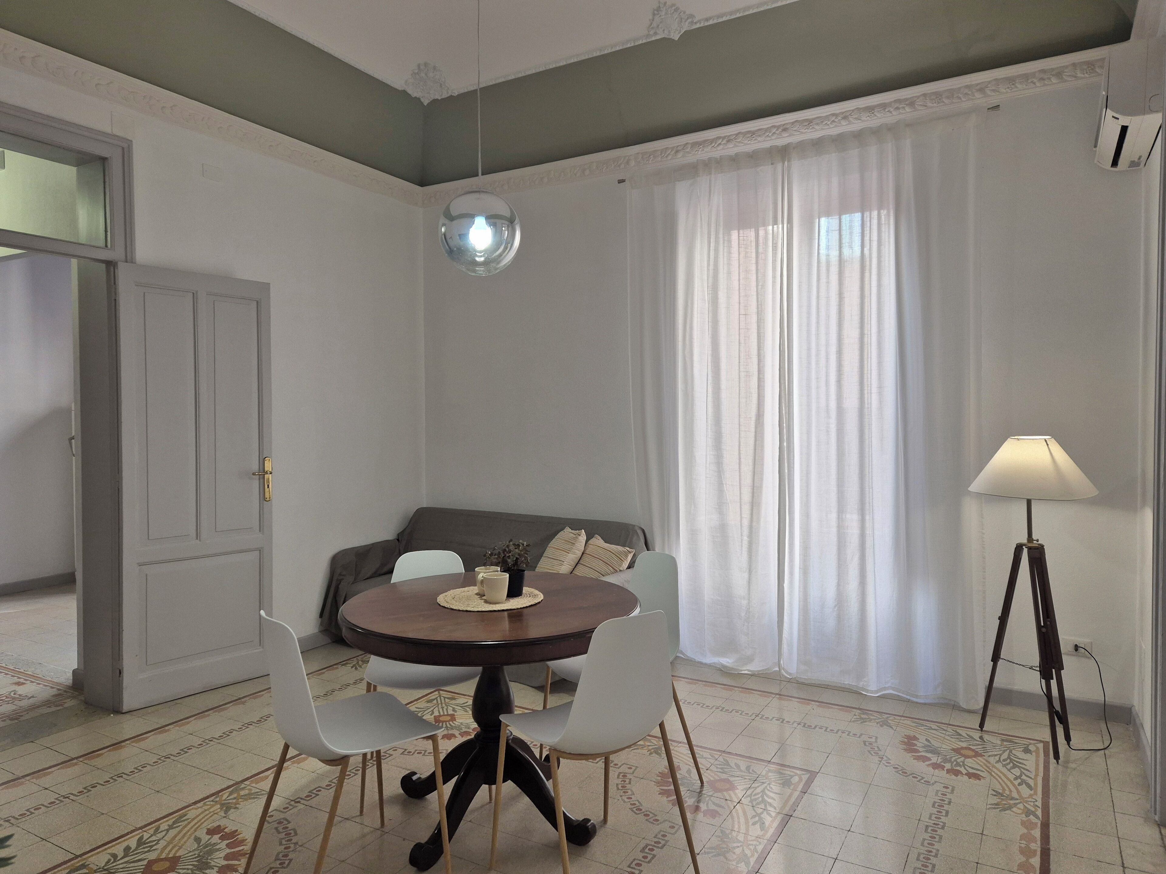 Ein Essbereich mit einem runden Tisch, vier Stühlen, einer Hängeleuchte, einer Couch und einer Stehlampe.