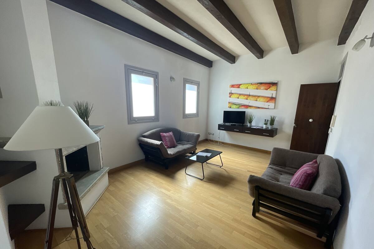 A living room with a sofa, armchair, coffee table, lamp, TV, and artwork on the wall.