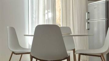 A modern room with a dining table and chairs, a kitchen area, and a window with sheer curtains.