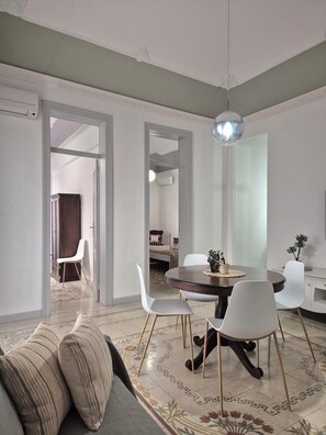 A modern living room with a round dining table, white chairs, a sofa with striped cushions, and a patterned rug. - CASE VACANZE LA MATTANZA (Trapani)