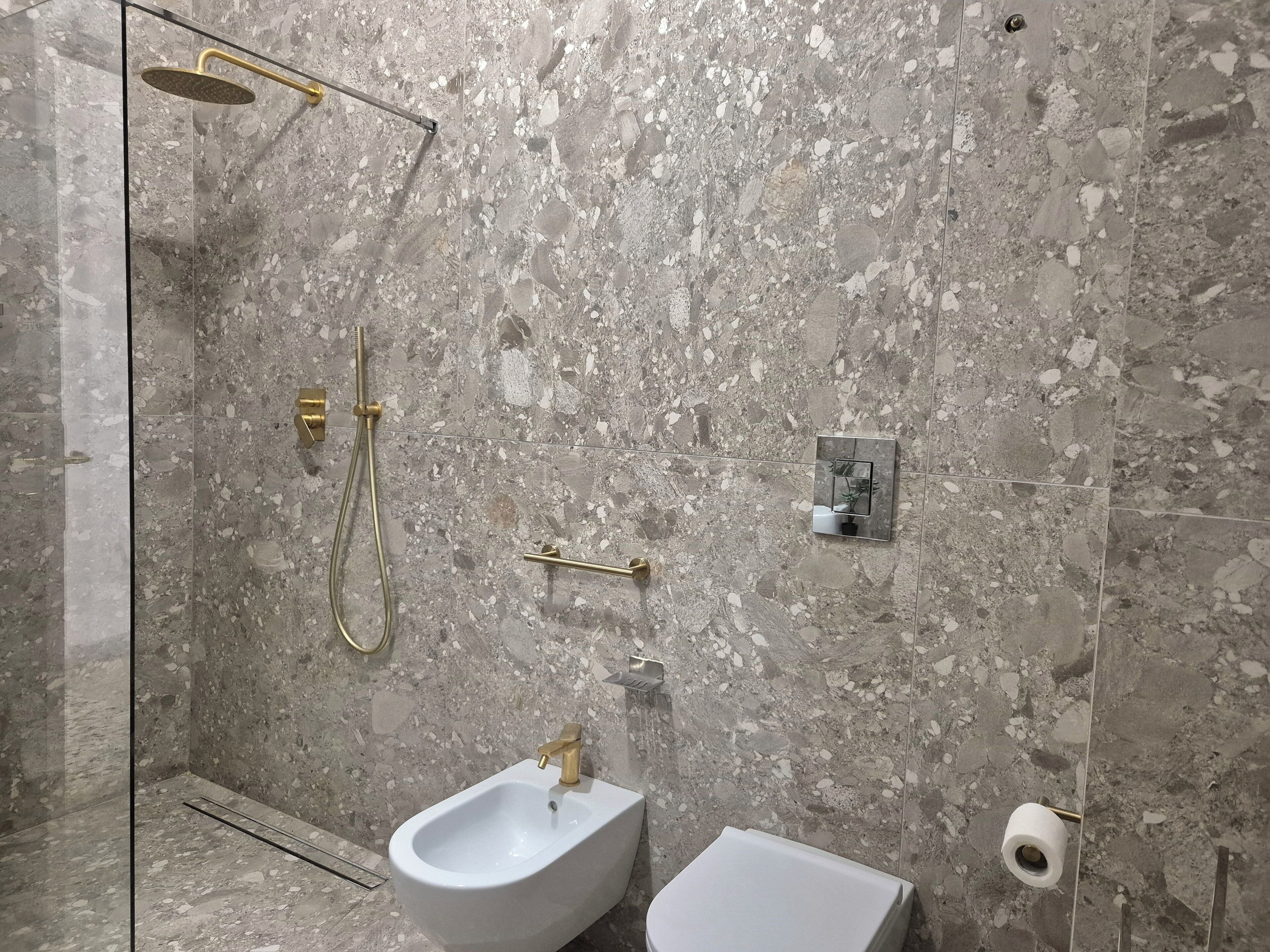 Un baño con ducha, bidé, inodoro y paredes de mármol.