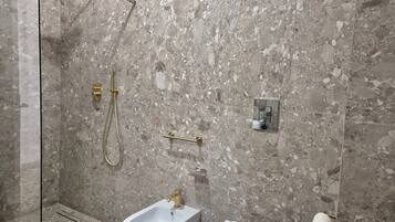 Un baño con ducha, bidé, inodoro y paredes de mármol.