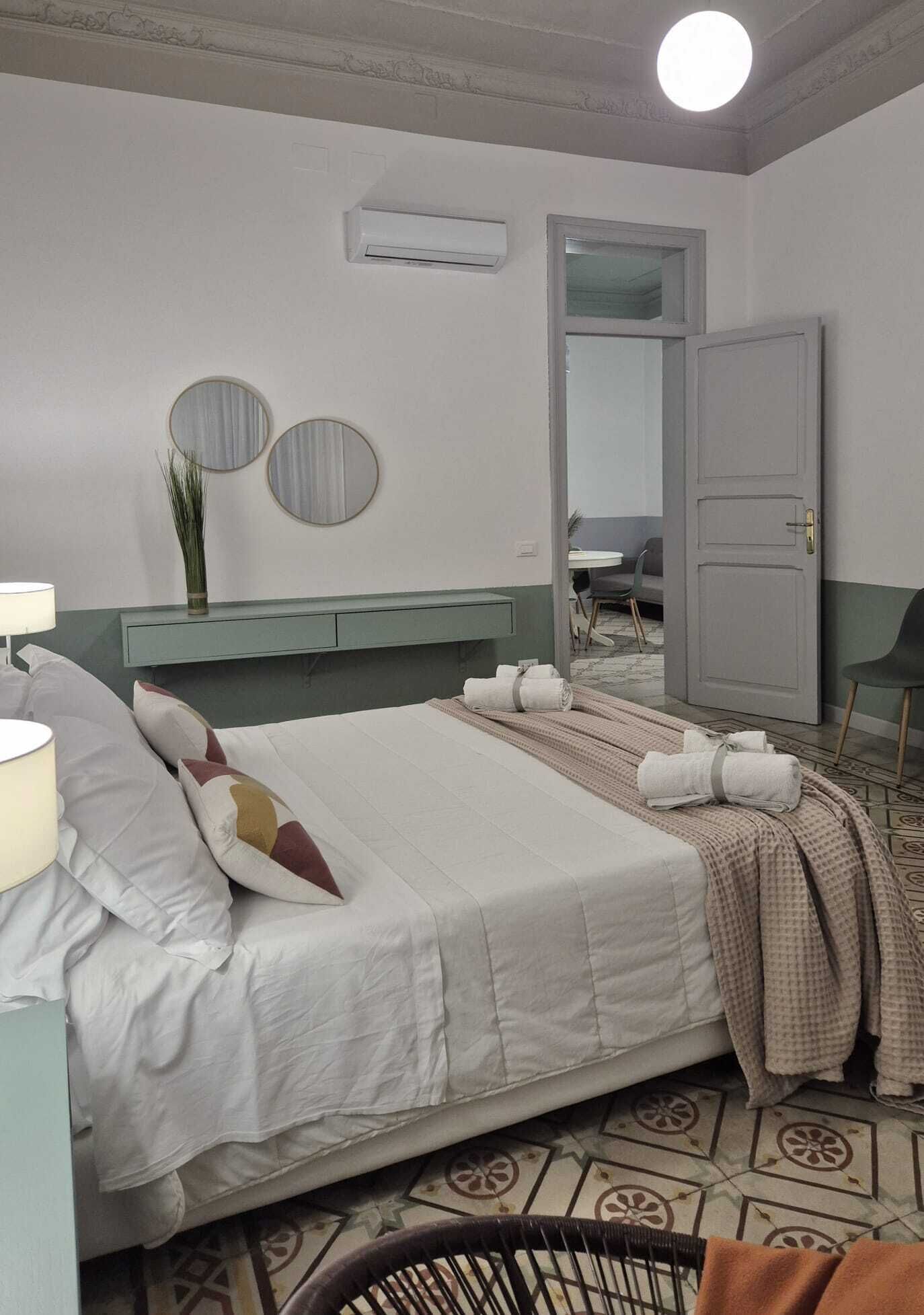 Una cama bien hecha con toallas, una lámpara de noche y un espejo en la pared.