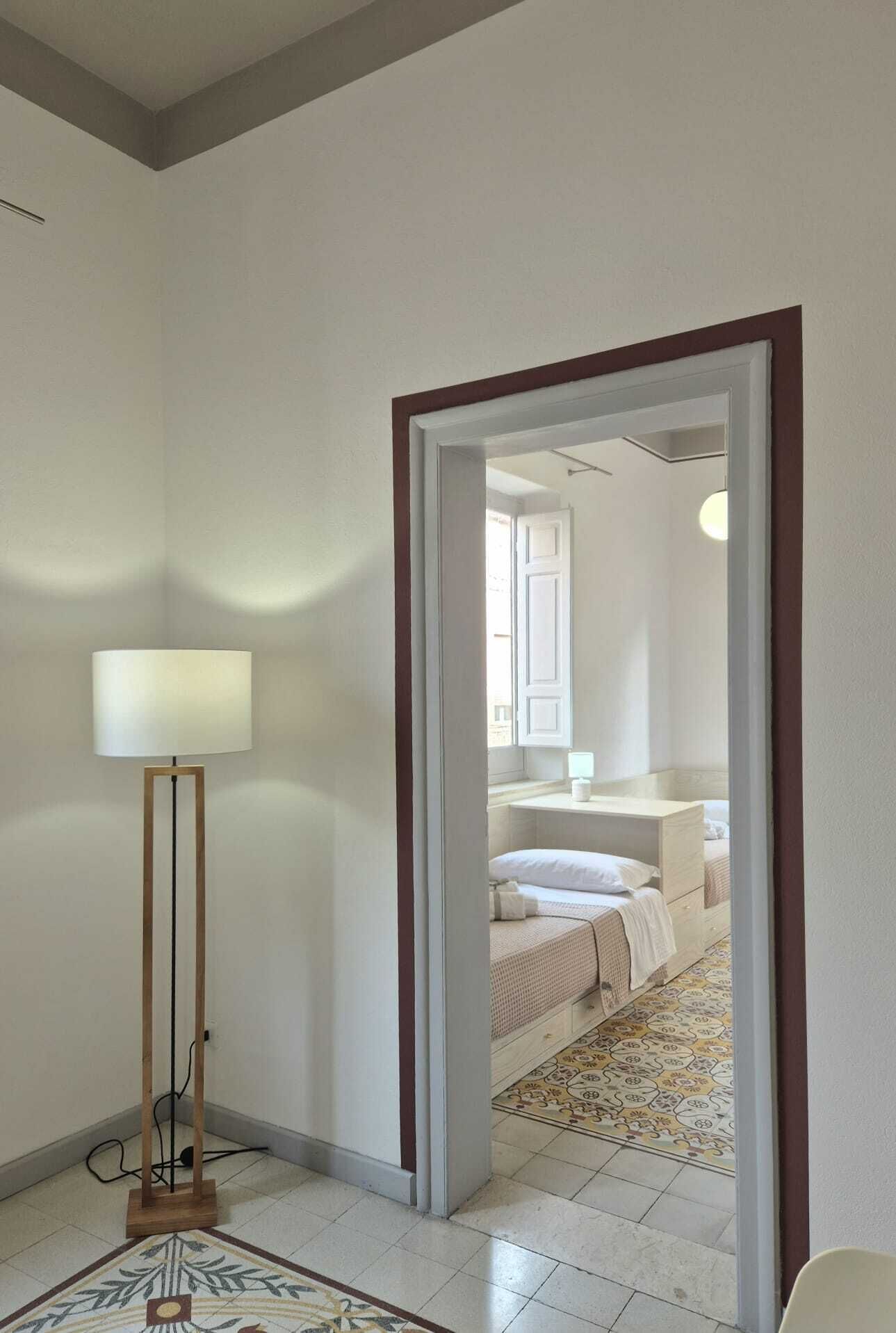 Un pasillo que conduce a un dormitorio con una cama, una mesita de noche y una lámpara.