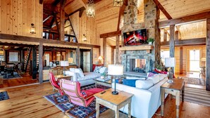 A spacious living room with a stone fireplace, wooden beams, and a cozy seating area with a white sofa and a red chair. - The Chateau at Timberline (Davis)