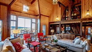 A spacious living room with wooden walls and large windows, a red armchair, a white sofa, and a coffee table with books. - The Chateau at Timberline (Davis)
