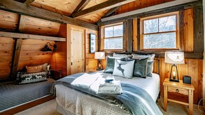 A cozy cabin-style bedroom with a bed, bedside tables, and a window with a view of trees. - The Chateau at Timberline (Davis)