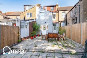 A courtyard with a patio table and chairs, surrounded by a wooden fence and potted plants. - Omega @ Hanwell | Ground Floor Ensuite | Parking (London)