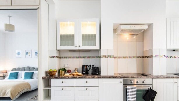 A modern kitchen with white cabinets, a stove, and a coffee maker.