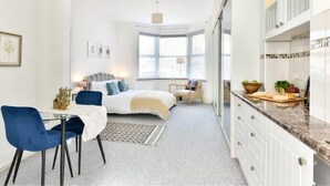 A modern hotel room with a dining area, a bed with a view, and a kitchen counter.